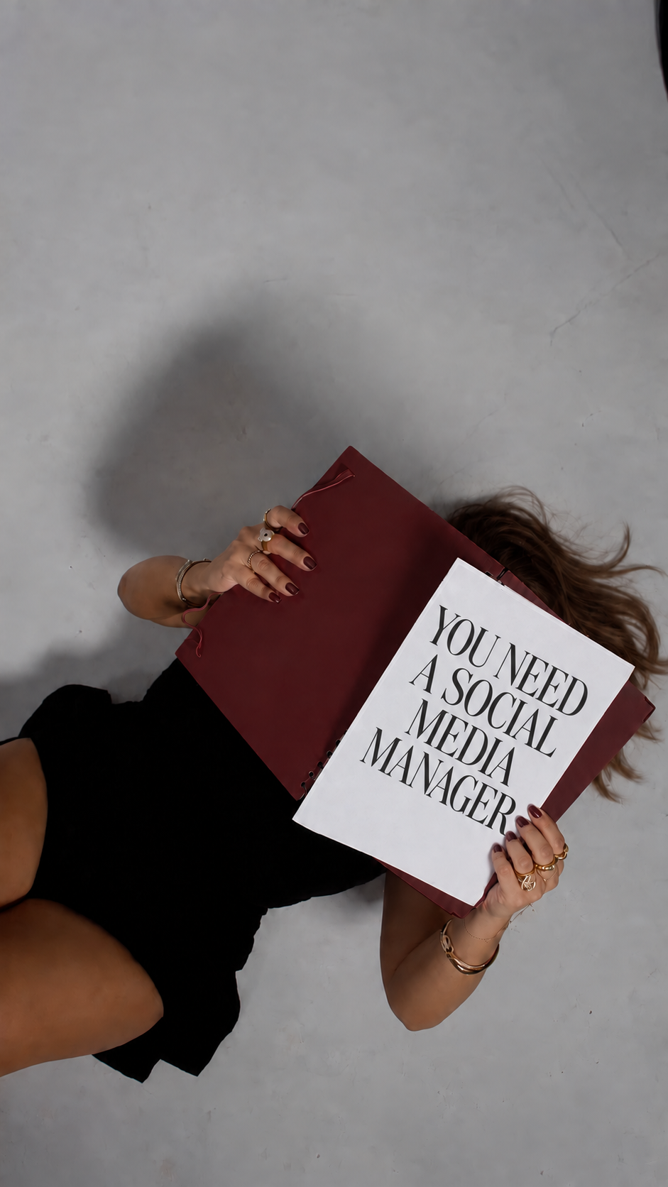 Woman with long brown hair holding a paper that reads You Need a Social Media Manager